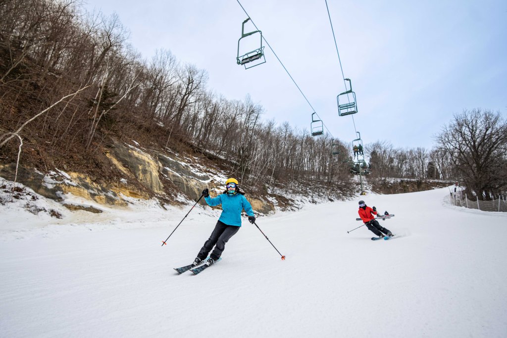 two people skiing in the snow under a chairlift