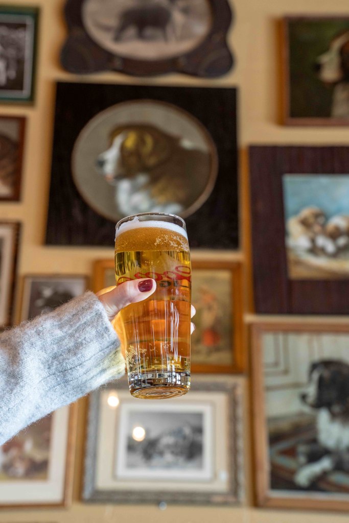 a hand holding up a beer in front of a wall of Saint Bernard portraits