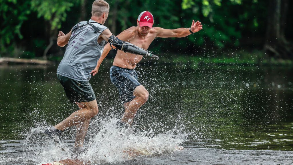 A person in a hat and a person with a prosthetic arm jumping into a lake