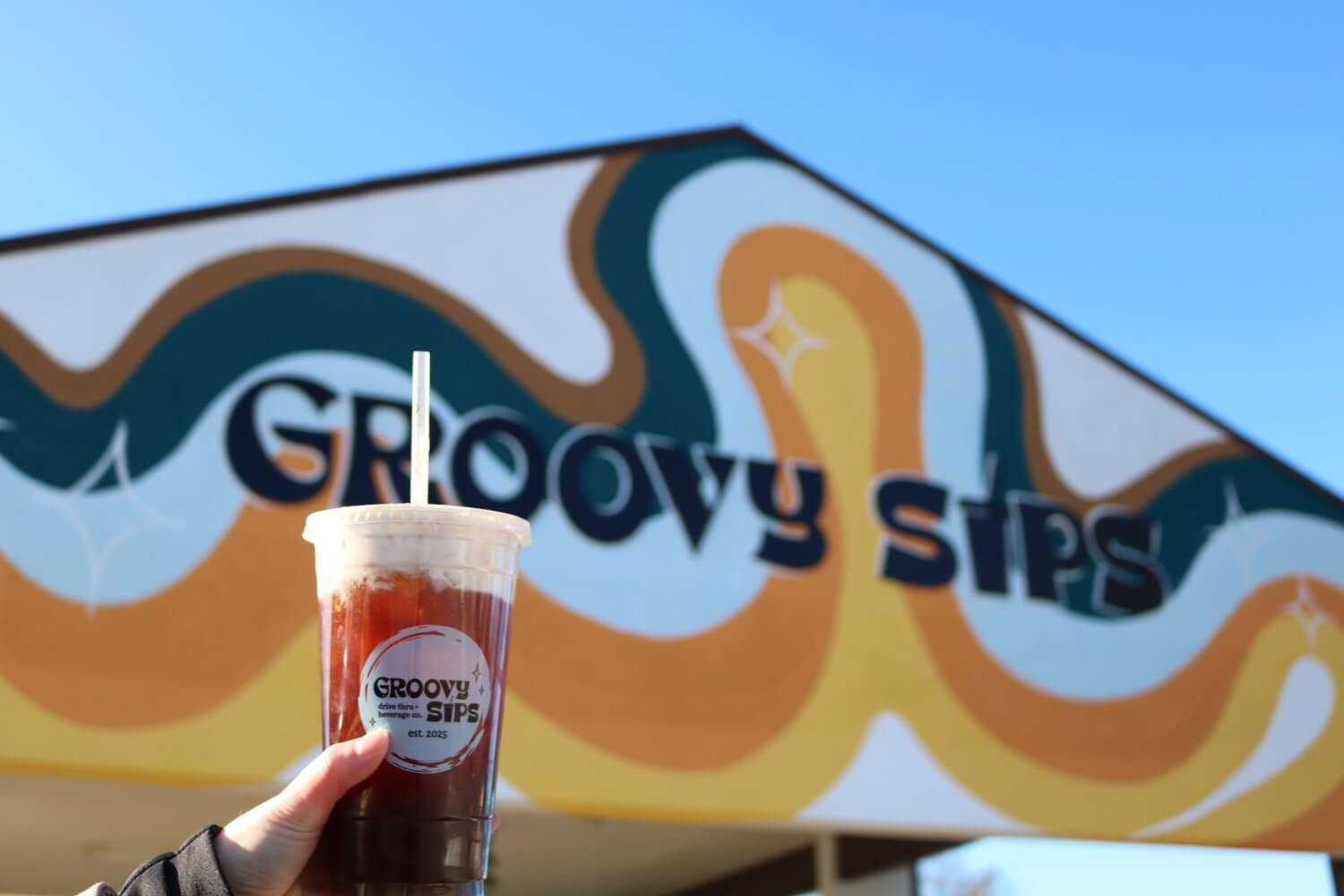 Top 10 Local Coffee Shops For A "Brewtiful" Day A dirty soda held in front of the Groovy Sips Storefront