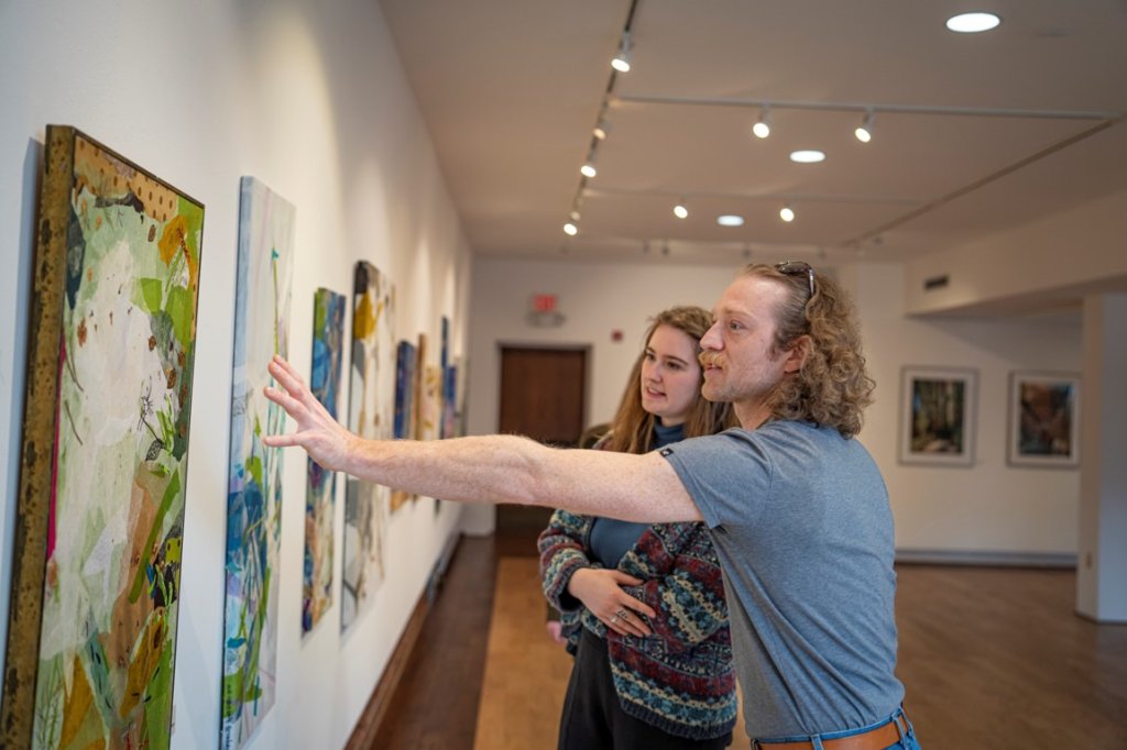 Two people, one person reaching their hands out to a painting as they discuss the art piece
