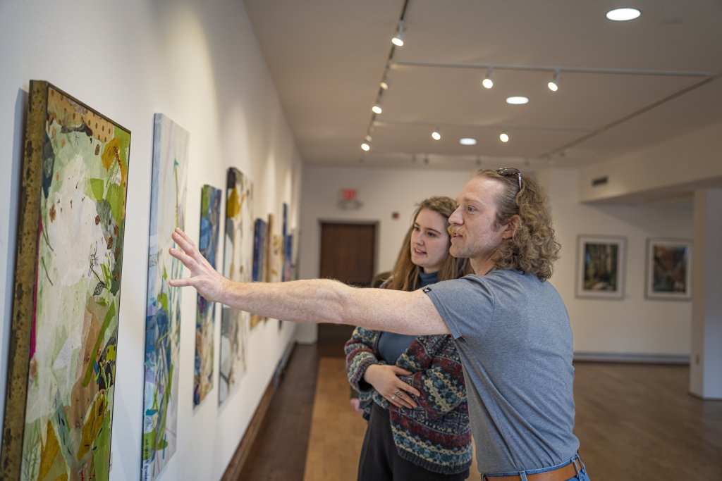 Two people, one person reaching their hands out to a painting as they discuss the art piece