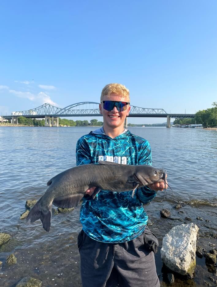 a man holding a fish in front of a river