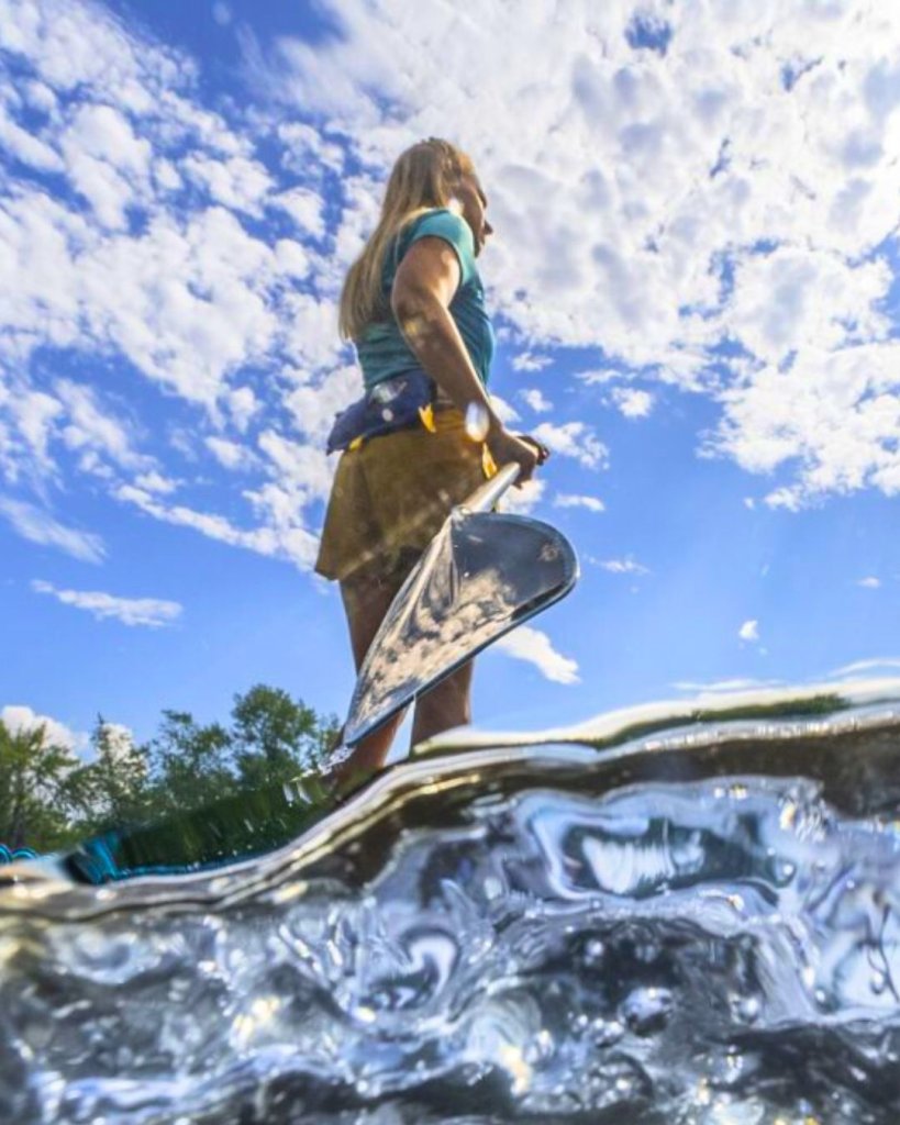 Freshwater covers the bottom of the frame as a woman stands on her paddleboard, facing away from the camera, in beautiful La Crosse, Wisconsin.