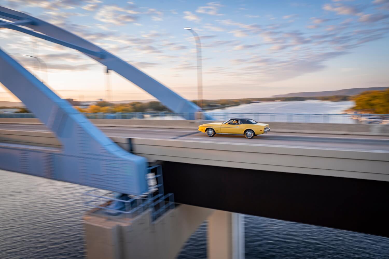 A yellow car travels on a bridge over a river in beautiful La Crosse, Wisconsin at sunset.