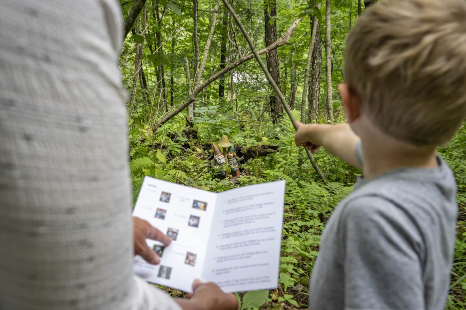 a man and boy looking at a book in the woods