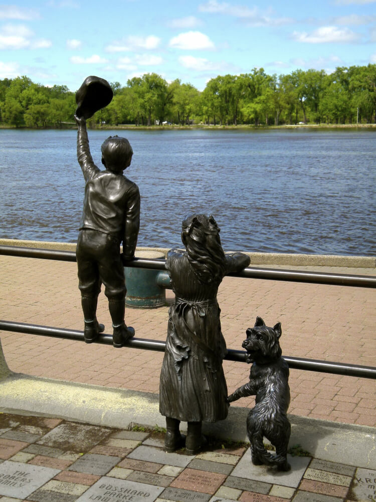 a statue of a boy and girl holding a hat and standing on a railing