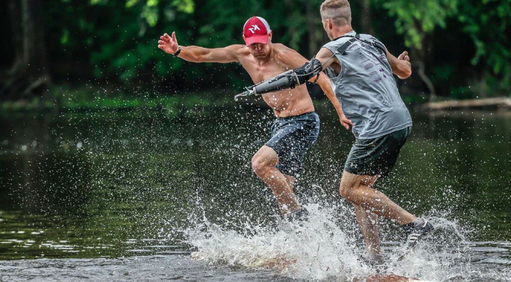 Sports Events 9 A person in a hat and a person with a prosthetic arm jumping into a lake