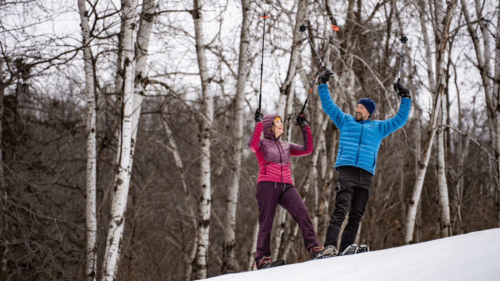 A couple cross country skiing with their poles in the air in celebration