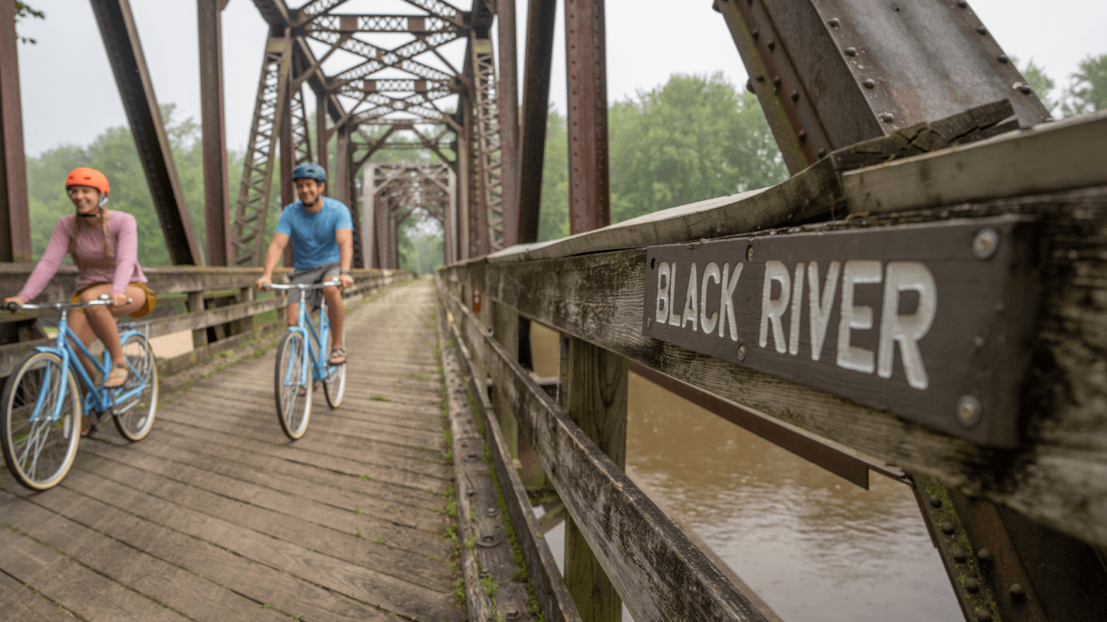 a couple biking over a bridge of the black river