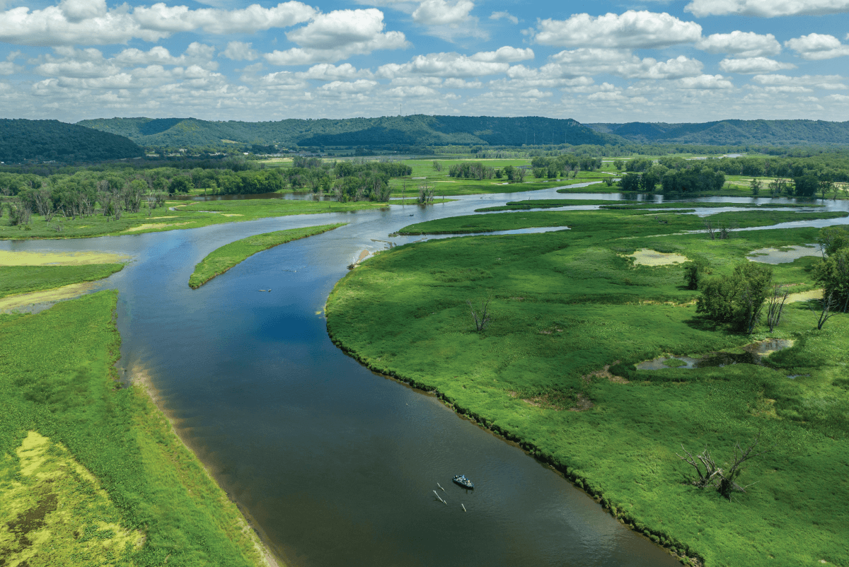Aerial view of the Mississippi River winding through the La Crosse Region in Wisconsin’s Driftless Area, with anglers in a boat, cruising around and surrounded by lush green bluffs and scenic backwaters.
