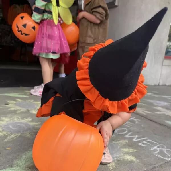 child in Halloween costume reaching into bucket for candy